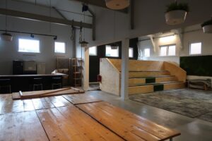 Interieur van een moderne multifunctionele ruimte aan het Gedempt Hamerkanaal met houten banken, hoge plafonds en hangplanten.